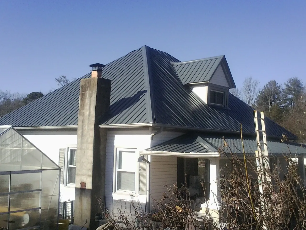 Dark blue standing seam metal roof on a white farmhouse with dormer — Slate & Tile Roof Repair by Roofing Brothers in New Weston