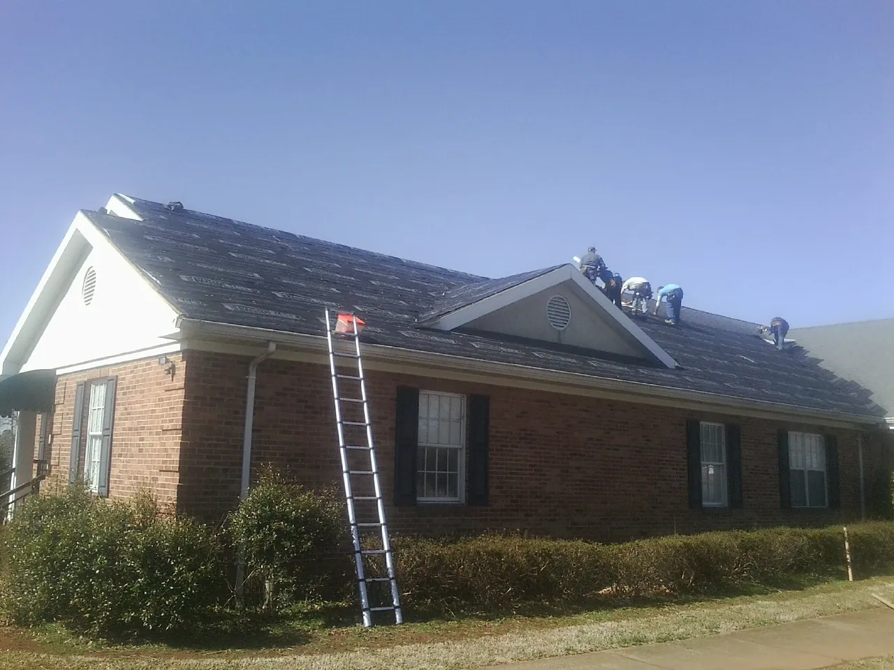 Crew tearing shingles off a brick ranch roof with a ladder set — Metal Roof Repair work by our crew in New Weston
