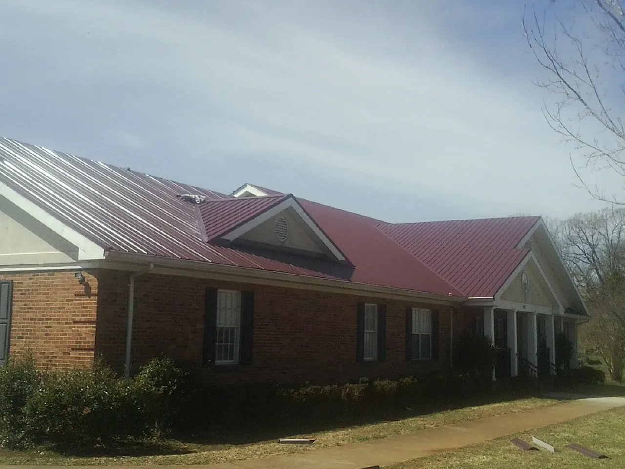 Red metal roof with gabled entries on a long brick building, from a Hail Damage Roof Repair job in New Weston