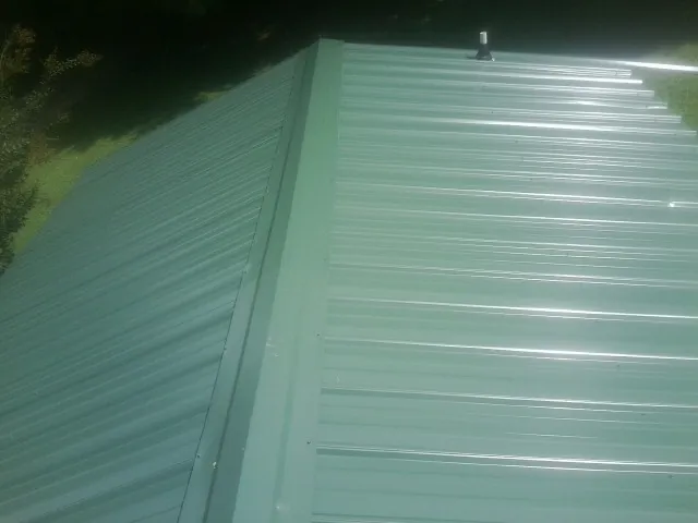 New green metal panels meeting at the ridge of a roof — Flat Roof Repair work by our crew in New Weston
