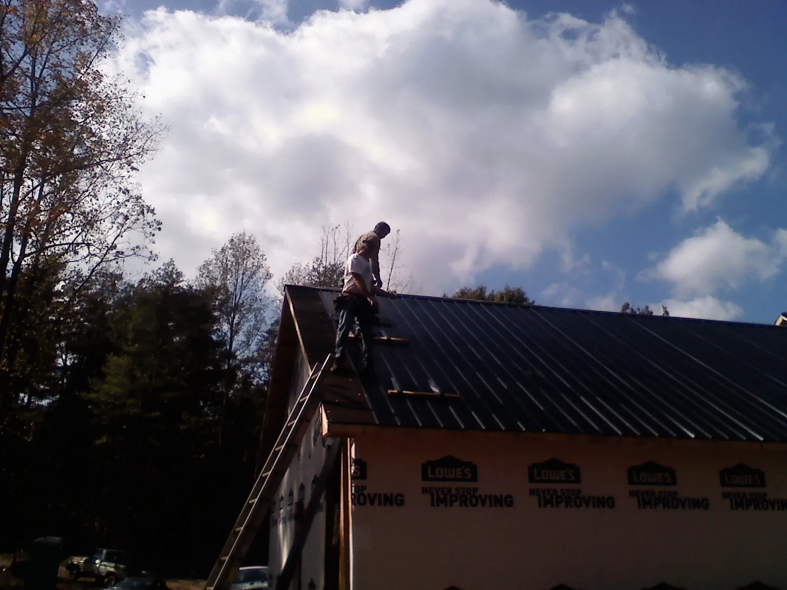 Roofer fastening dark metal panels high against a cloudy sky, from a Roof Inspection job in New Weston