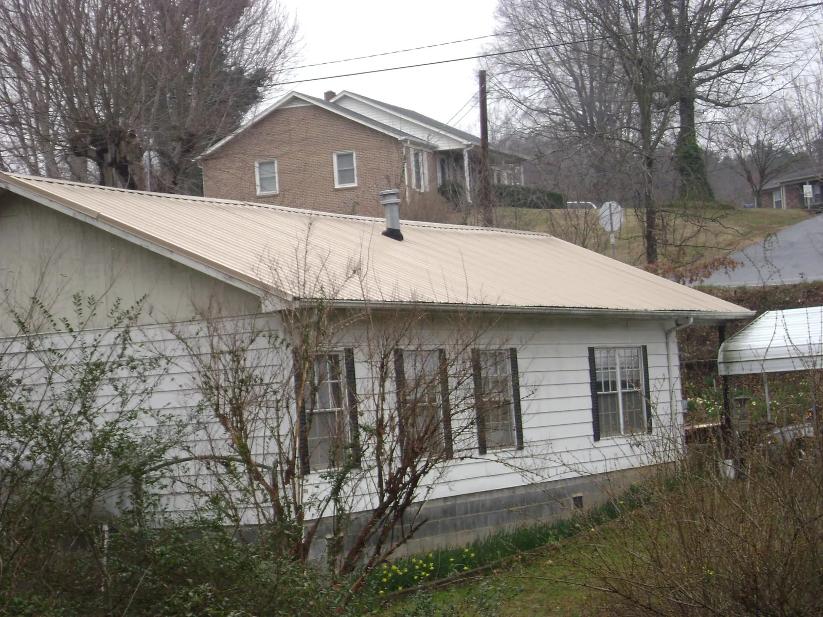 Tan metal roof on a white sided house set into a hillside — Commercial Roofing by Roofing Brothers in New Weston