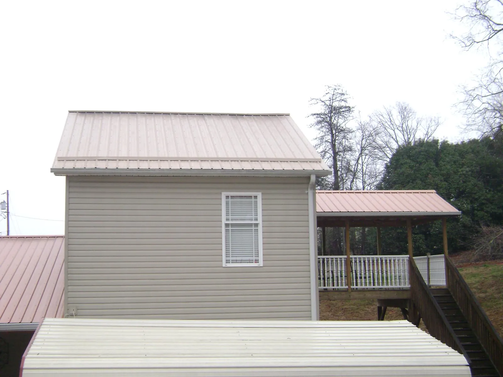 Tan metal roofs on a two story addition and attached porch, from a Roof Replacement job in New Weston