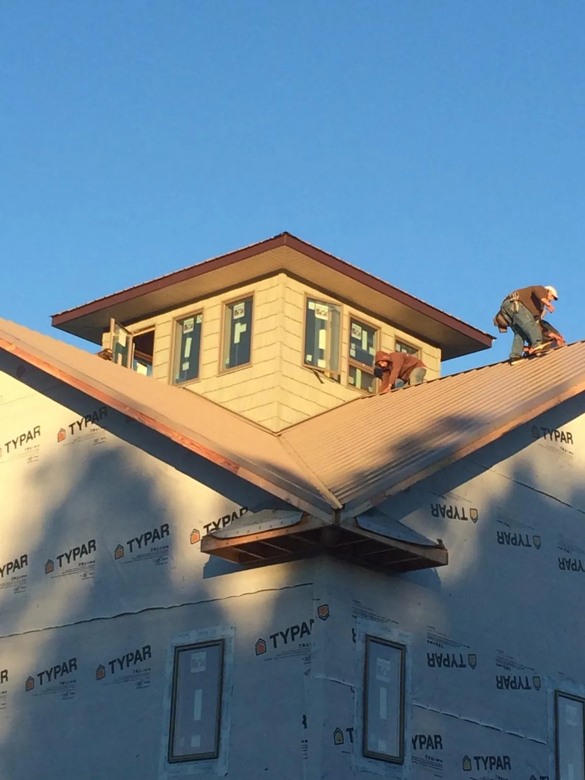 Roofers working around a rooftop cupola on a new metal roof at sunset in New Weston
